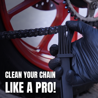 A close-up of a hand wearing a black glove holding a black chain cleaning brush in front of a motorcycle chain and red wheel, with the text 'CLEAN YOUR CHAIN LIKE A PRO!' overlaid at the bottom.